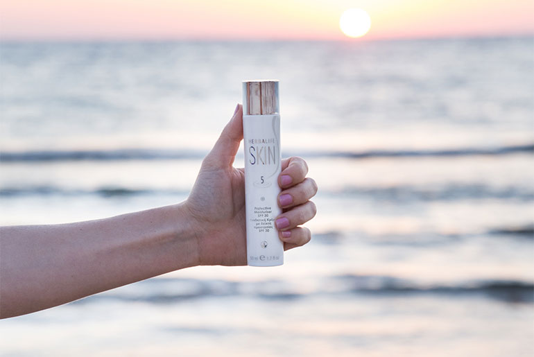 Kvinna som håller i en Herbalife SKIN-produkt för sommarhudvård